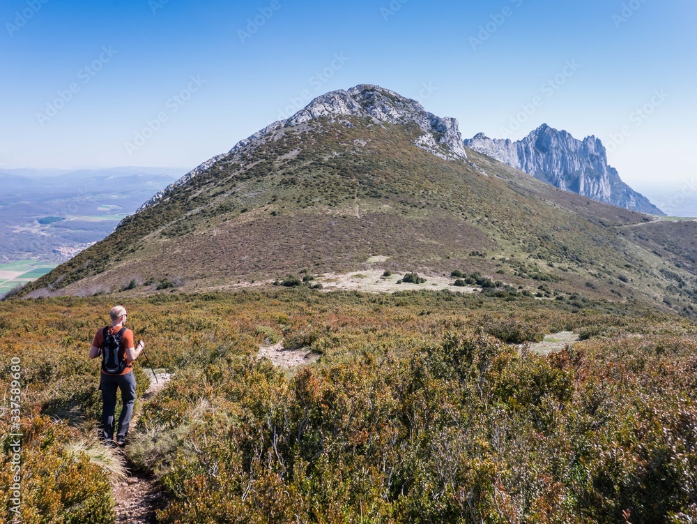 Male hiker descending a mountain and view over peak Recilla in the Cantabria mountain range between La Rioja and Alava, Basque Country, Spain