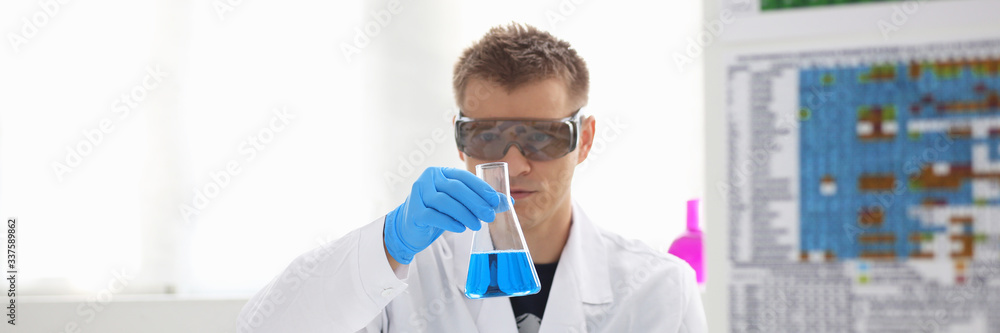 A male chemist holds test tube of glass in his hand overflows a liquid solution of potassium permanganate conducts an analysis reaction takes various versions of reagents using chemical manufacturing A male chemist holds test tube of glass in his hand overflows a liquid solution of potassium permanganate conducts an analysis reaction takes various versions of reagents using chemical manufacturing