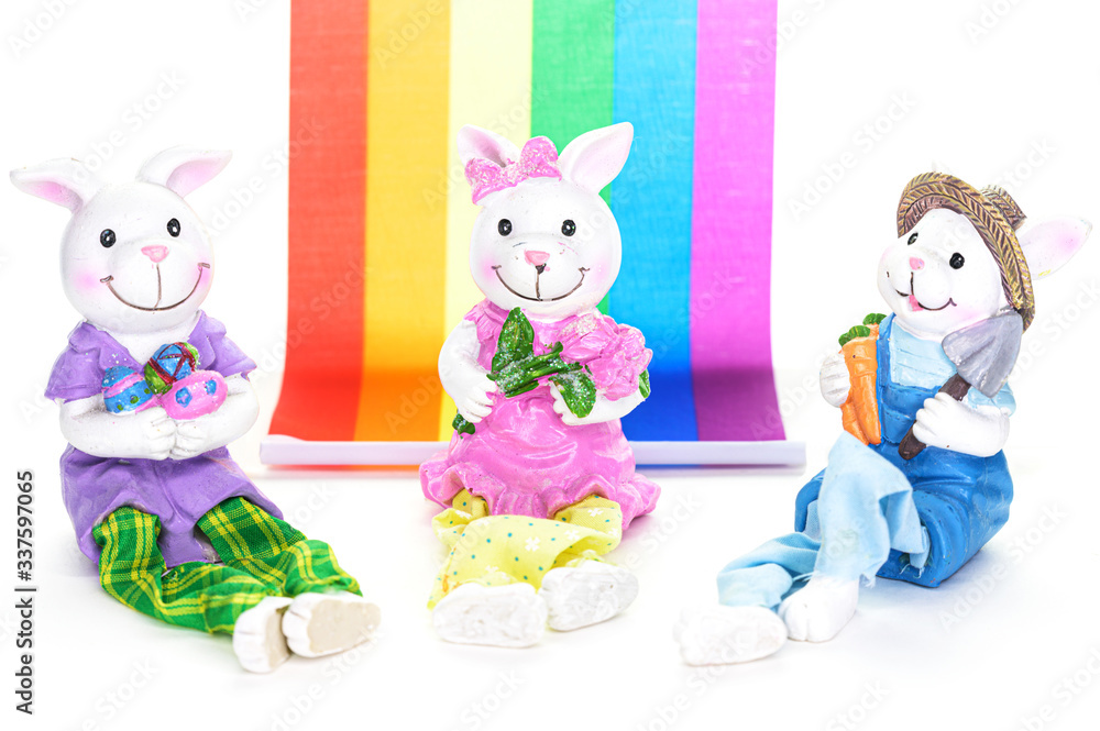 Three cute porcelain bunny rabbits ready for the Easter holiday, in front of a rainbow flag