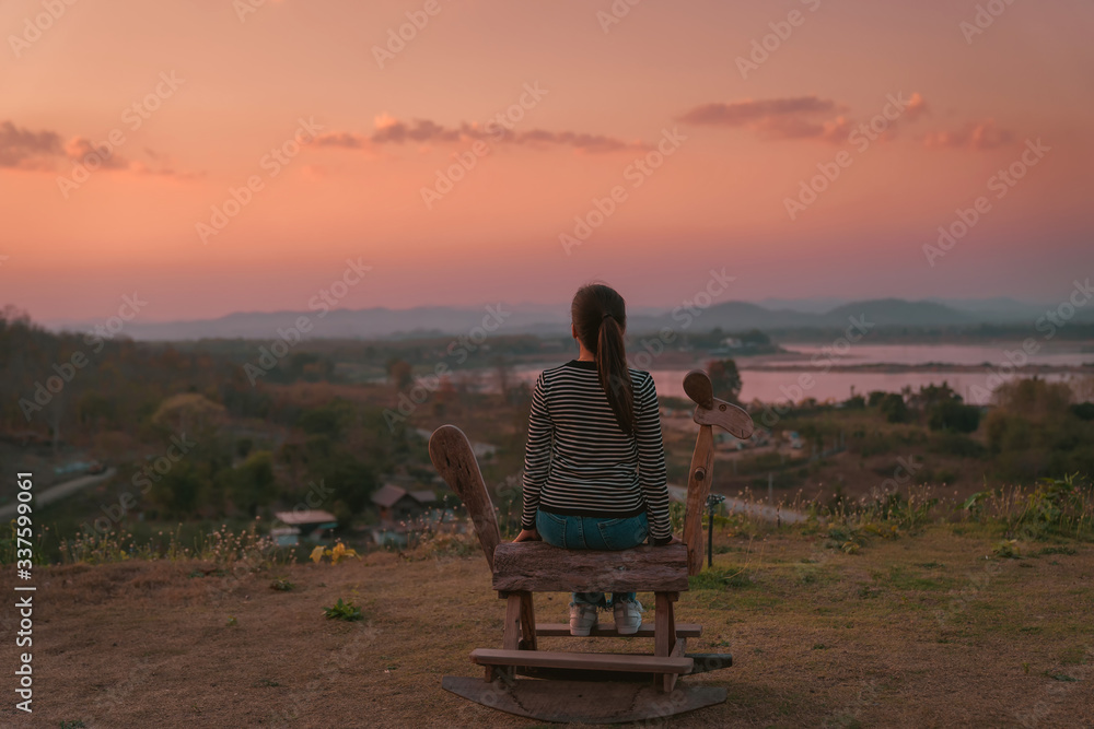 back side view hipster girl posing sit on Rocking horse toys with lonely emotional holiday on the mountain in sunset at Northeast at Chiangkhan of Thailand