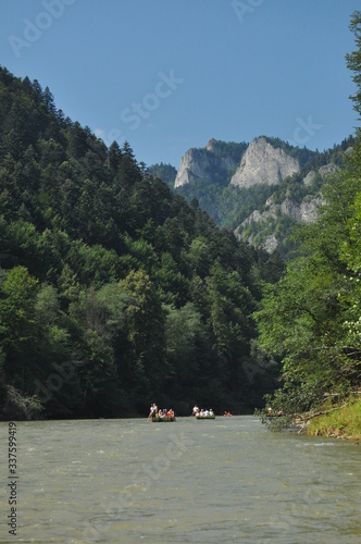 Rafting on the Dunajec River in the Pieniny National Park on wooden folding shuttles tied with a rope. Rafters paddling on a rapid stream with a rocky bottom and strong river current.