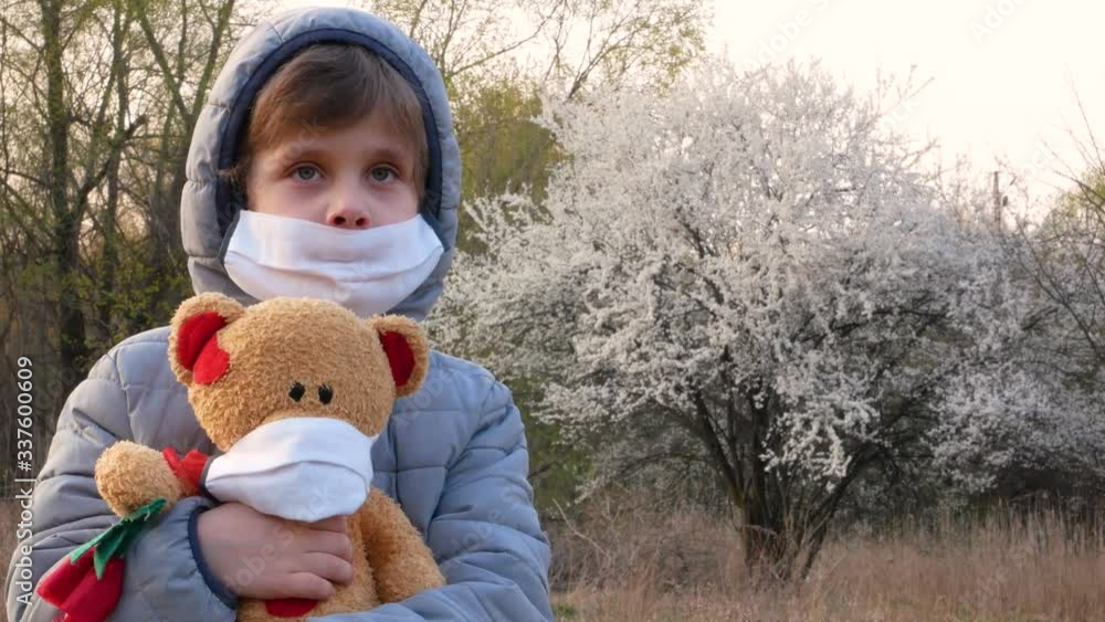 A cute boy 5-6 years old in a protective mask walks with a Teddy bear. Sad boy dressed in a protective mask. In the background is a tree with white flowers. Quarantine. Covid Coronavirus Pandemic 2019 A cute boy 5-6 years old in a protective mask walks with a Teddy bear. Sad boy dressed in a protective mask. In the background is a tree with white flowers. Quarantine. Covid Coronavirus Pandemic 2019