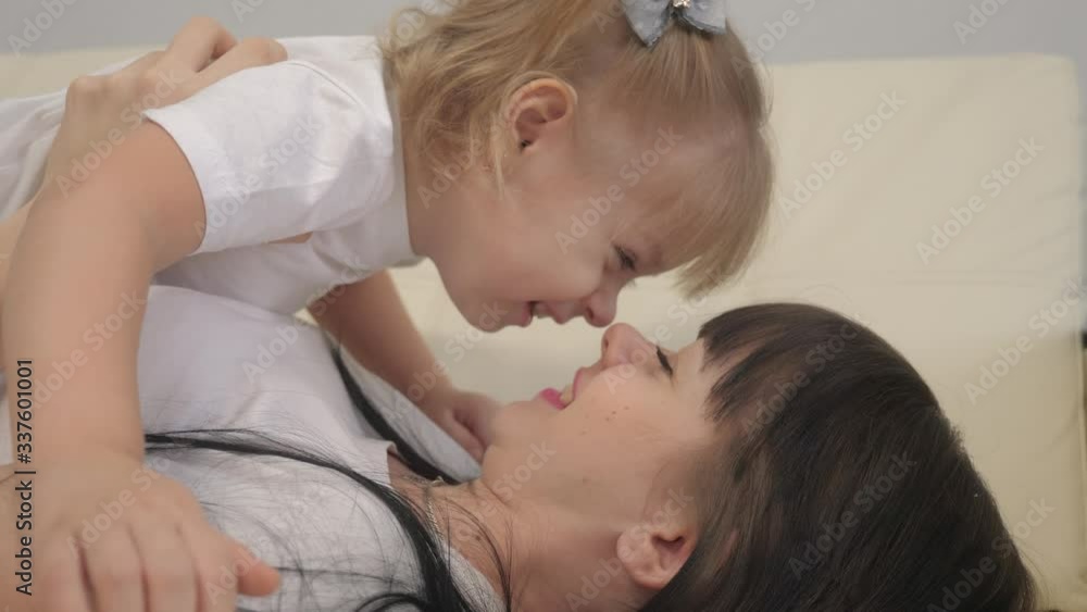 happy family concept .woman playing with a little girl on the bed. Mother lifestyle lies on her back and holds her daughter on her feet. mom kisses daughter laughing teamwork happy family concept .woman playing with a little girl on the bed. Mother lifestyle lies on her back and holds her daughter on her feet. mom kisses daughter laughing teamwork