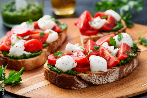 Tableau sur toile Bruschetta with cherry tomatoes,  mozzarella cheese and pesto sauce on wooden board