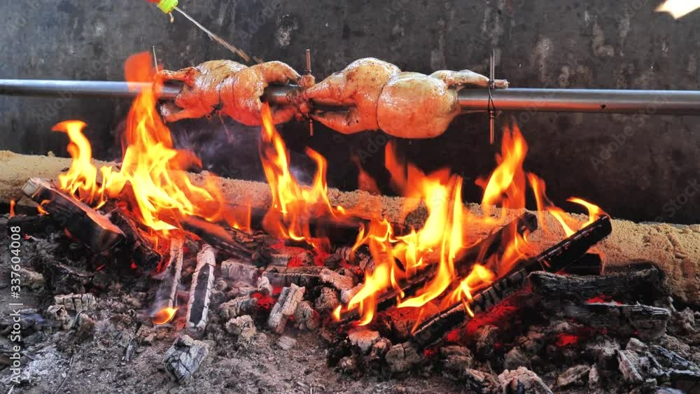 Man chef spray spicy marinate on roast Chicken on the BBQ steel bar in bricks built grill furnace. Man chef spray spicy marinate on roast Chicken on the BBQ steel bar in bricks built grill furnace.