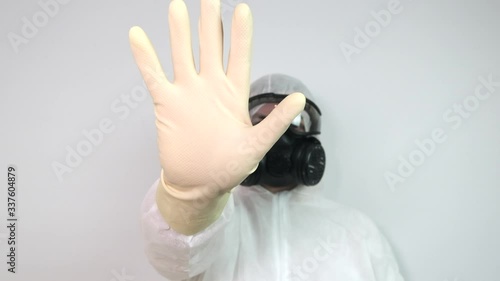 Male wearing protective suit, gas mask and goggles as protection against virus infection raises hand in stop gesture. Slow motion. photo