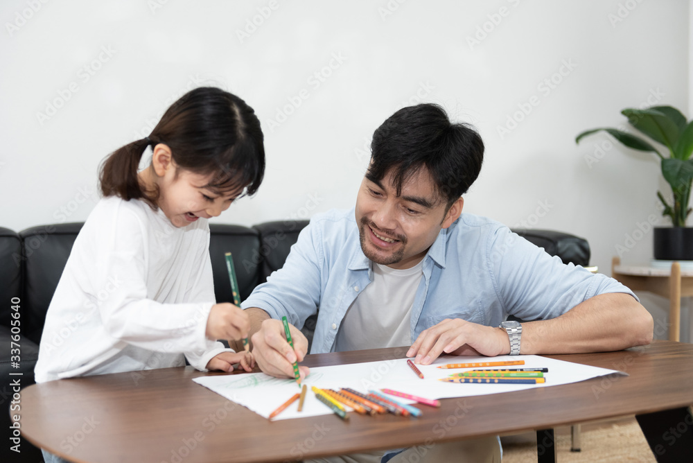 A pair of young Asian father and daughter are drawing in the living room A pair of young Asian father and daughter are drawing in the living room