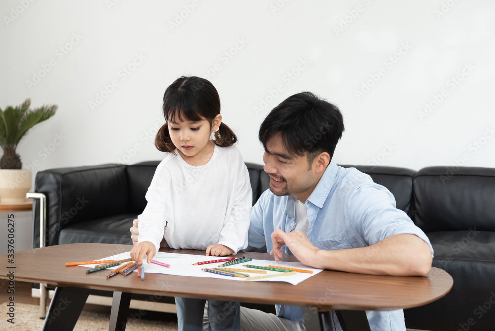 A pair of young Asian father and daughter are drawing in the living room A pair of young Asian father and daughter are drawing in the living room