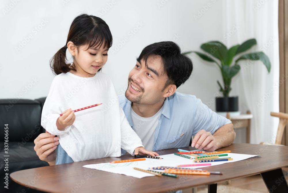A pair of young Asian father and daughter are drawing in the living room A pair of young Asian father and daughter are drawing in the living room