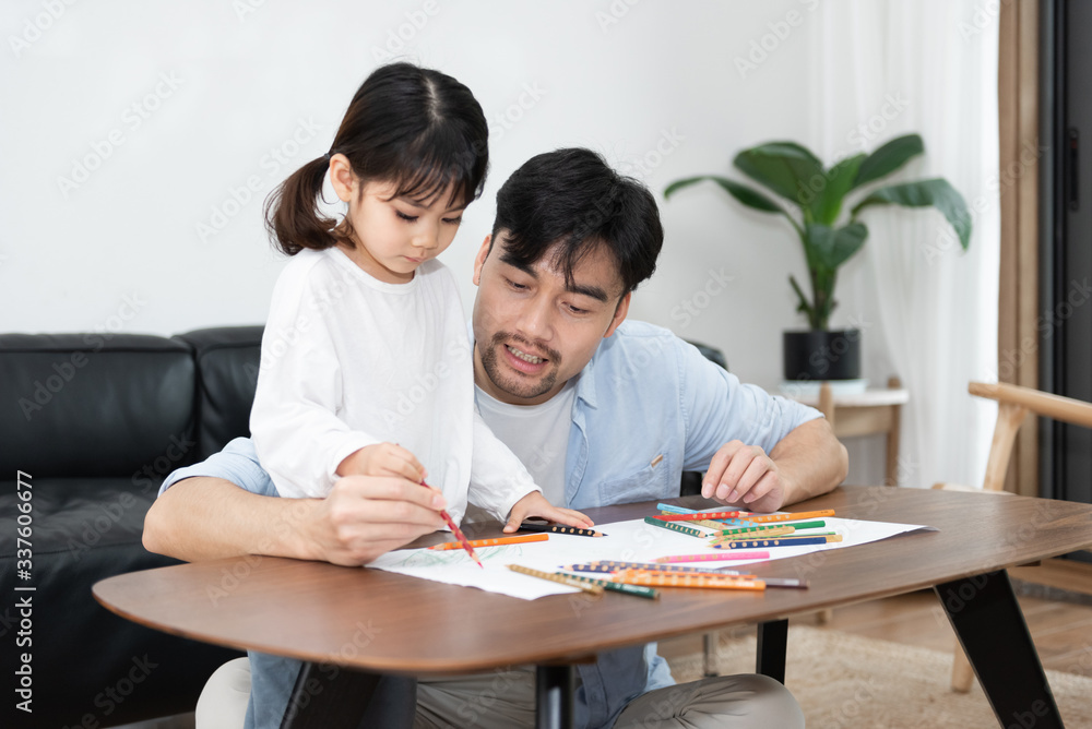 A pair of young Asian father and daughter are drawing in the living room A pair of young Asian father and daughter are drawing in the living room