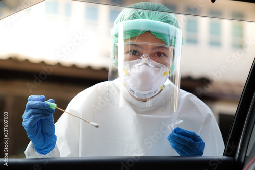 Doctor or nurse wearing PPE, N95 mask, face shield  and personal protective gown standing beside the car/road screening for Covid-19 virus  photo