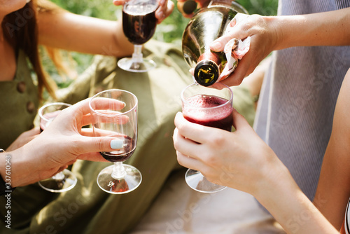 cropped image of girls or friends pouring red wine in glasses in park outdoor. close up. vine, rest, having fun concept
