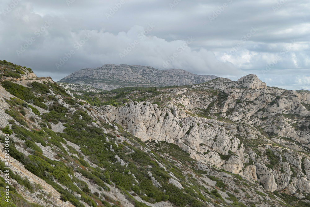 Mountains with green grass and grey rocks near the sea. Blue sky and white clouds.