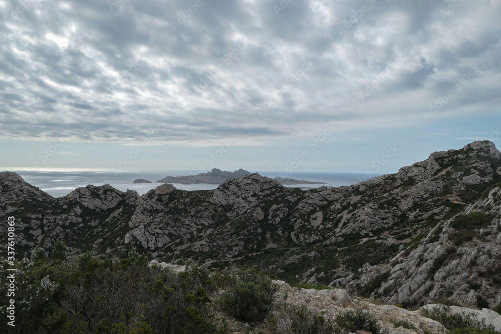 Mountains with green grass and grey rocks near the sea. Blue sky and white clouds. Mountains with green grass and grey rocks near the sea. Blue sky and white clouds.