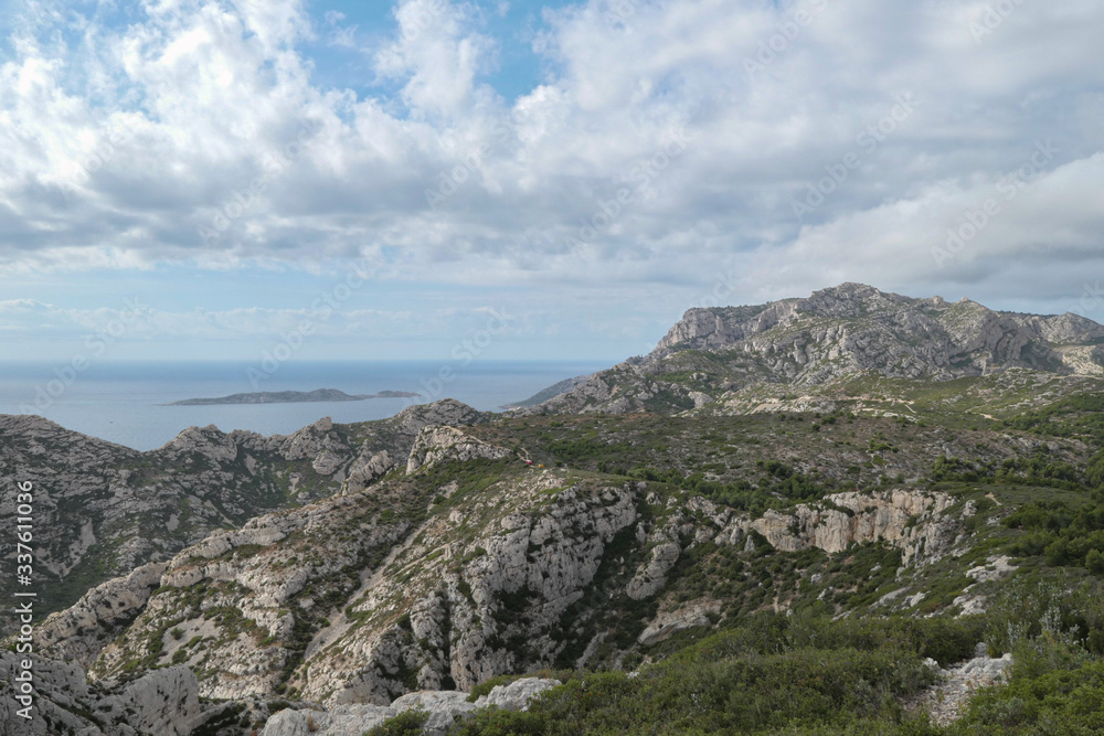 Mountains with green grass and grey rocks near the sea. Blue sky and white clouds. Mountains with green grass and grey rocks near the sea. Blue sky and white clouds.