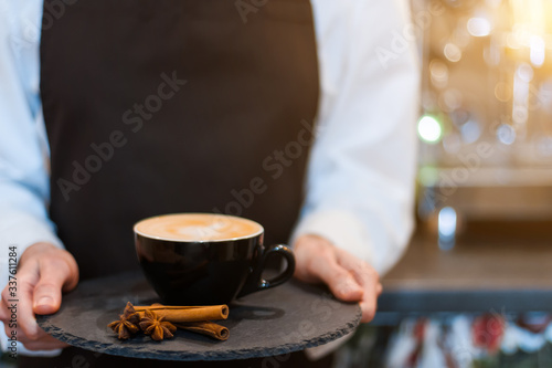 Closeup female hands are holding tray with cup of aromatic coffee with cinnamon. Barista woman prepared  brewed espresso  americano  latte cappuccino using professional machine in cafe  restaurant.