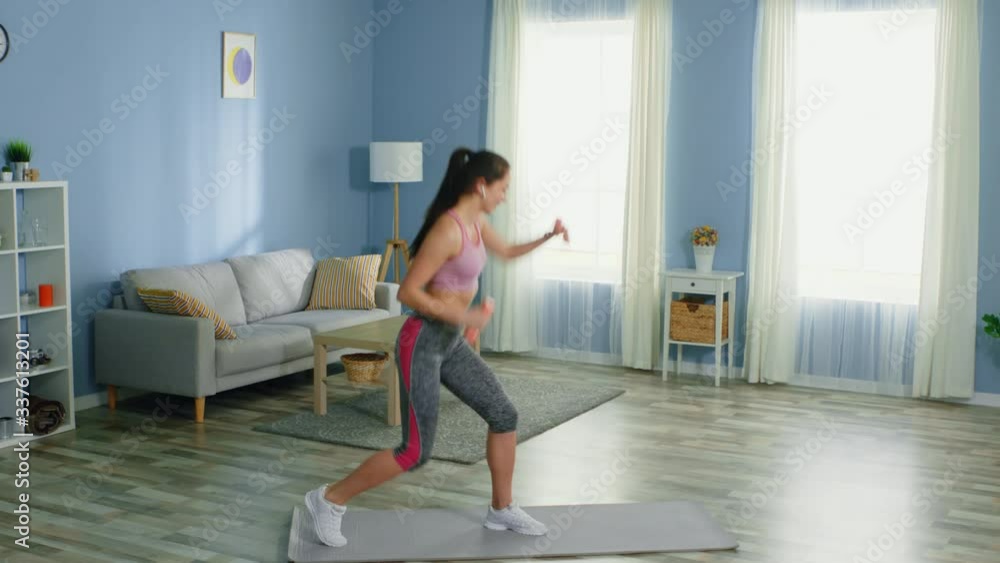 Young woman is training in the morning, using light dumbbells, staying positive and energetic, listening her favorite music, look at camera and smile, slow motion. Young woman is training in the morning, using light dumbbells, staying positive and energetic, listening her favorite music, look at camera and smile, slow motion.