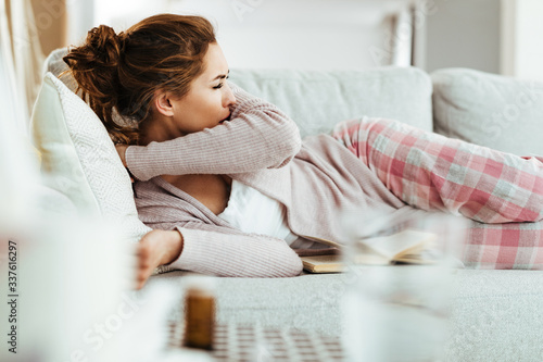 Young woman coughing into elbow while lying down on sofa in the living room. photo