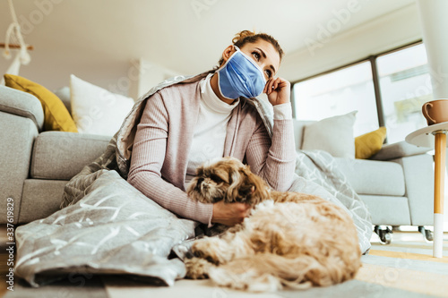 Below view of pensive woman wearing face mask while relaxing with her dog at home. © Drazen
