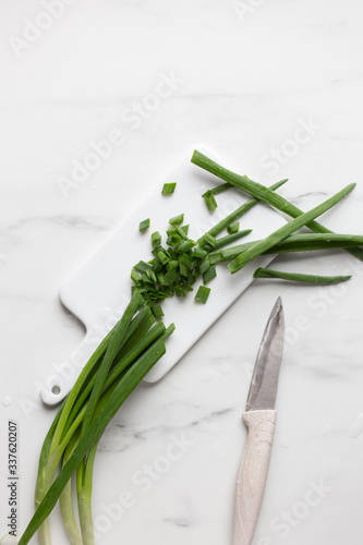 Whole and chopped green onions on white marble background