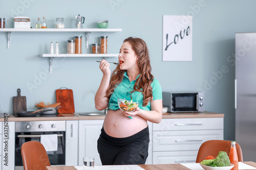 Beautiful pregnant woman with healthy salad in kitchen