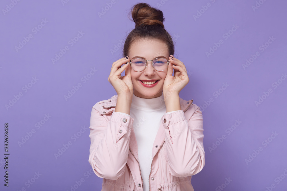 Image of good looking attractive young lady touching frame of her eyeglasses, looking directly at camera, smiling sincerely, having pleasant facial expression, being in good mood. Emotions concept. Image of good looking attractive young lady touching frame of her eyeglasses, looking directly at camera, smiling sincerely, having pleasant facial expression, being in good mood. Emotions concept.