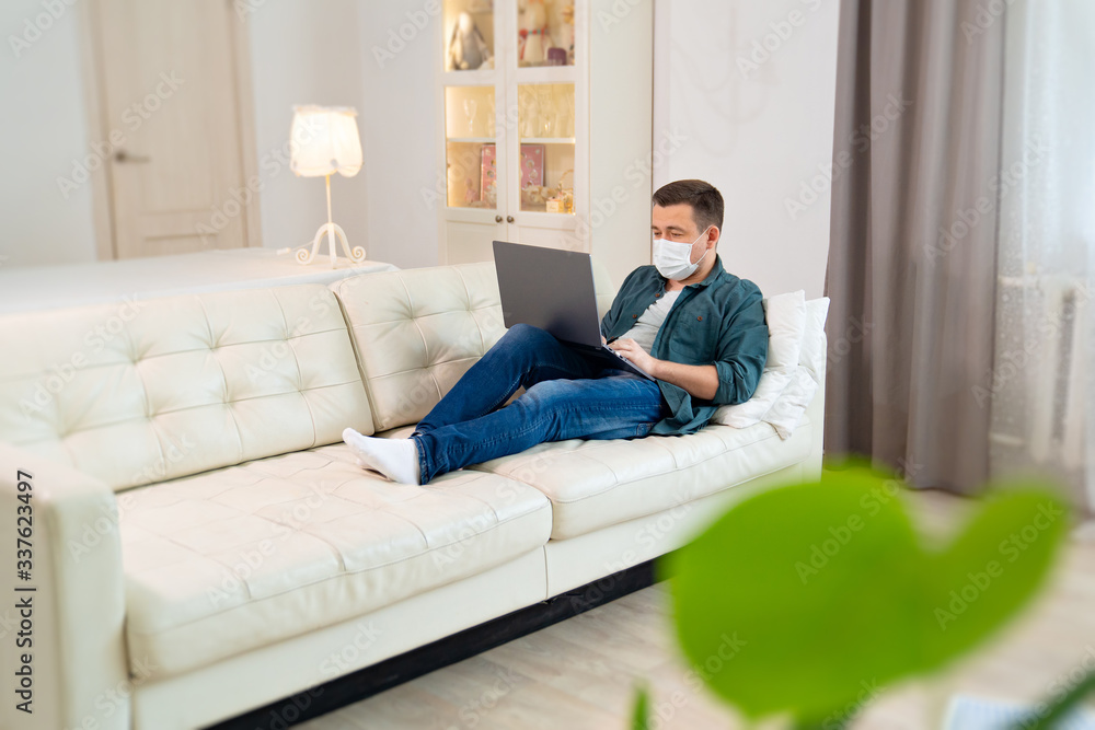 man freelancer in medical mask working on couch man freelancer in medical mask working on couch