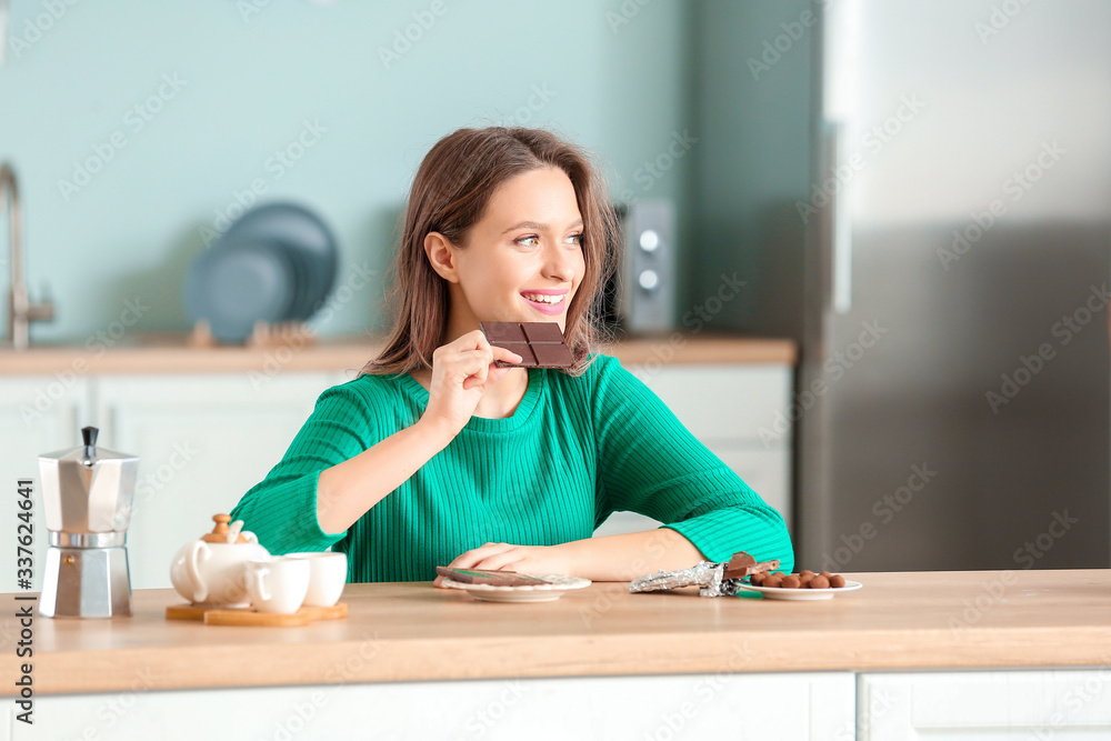 Beautiful young woman eating chocolate in kitchen Beautiful young woman eating chocolate in kitchen