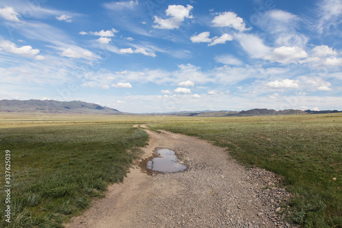 Charyn nature reserve steppe gravel road with puddle with cloudy sky near Almaty, Kazakhstan