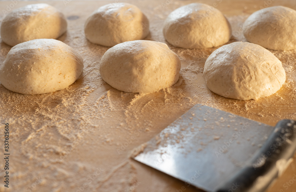 Stay at home for coronavirus covid-19 lockdown concept: make pizza at home. Backlit low angle view of leavened dough portions ready to bake on a light wooden work table dusted with flour Stay at home for coronavirus covid-19 lockdown concept: make pizza at home. Backlit low angle view of leavened dough portions ready to bake on a light wooden work table dusted with flour