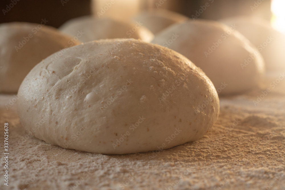 Stay at home for coronavirus covid-19 lockdown concept: make pizza at home. Backlit close-up of leavened dough portions ready to bake on a light wooden work table dusted with flour Stay at home for coronavirus covid-19 lockdown concept: make pizza at home. Backlit close-up of leavened dough portions ready to bake on a light wooden work table dusted with flour