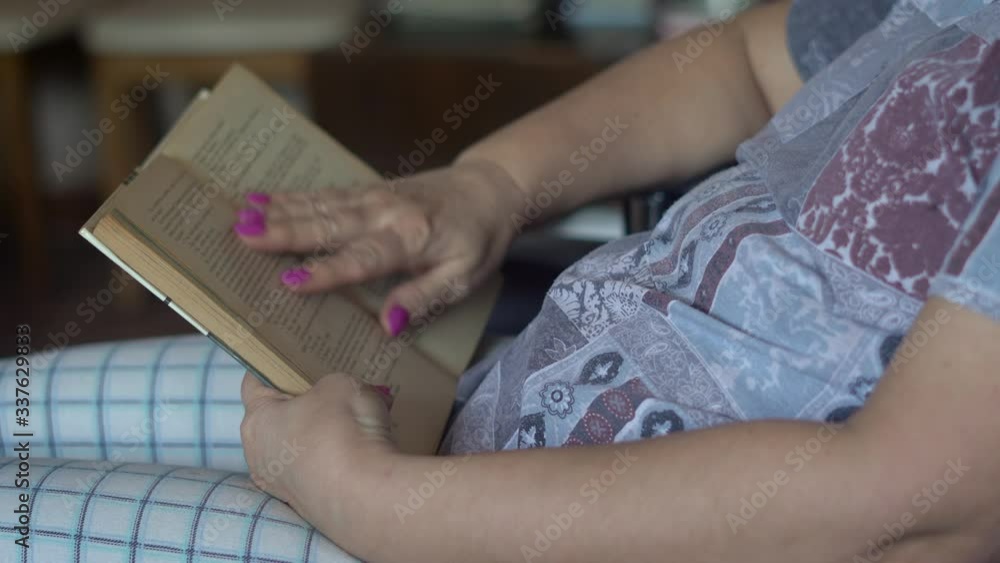 Grandma in a mask reading a book. She is in self-isolation at home during the coronavirus pandemic. She expects a volunteer to bring her food. Grandma in a mask reading a book. She is in self-isolation at home during the coronavirus pandemic. She expects a volunteer to bring her food.