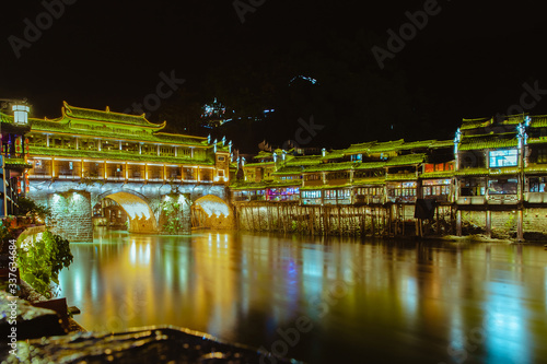 View of illuminated at night riverside houses and bridge in ancient town of Fenghuang known as Phoenix, China.