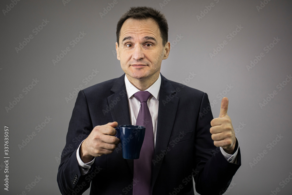 Good-looking male middle aged businessman in formal clothes, tie with cofee cup showing ok sign on isolated gray background, copy space. Portrait of handsome man, morning break, coffee time concept Good-looking male middle aged businessman in formal clothes, tie with cofee cup showing ok sign on isolated gray background, copy space. Portrait of handsome man, morning break, coffee time concept