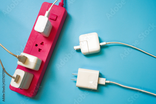 Pink extension power strip with only one socket left while there are 2 white mobile charger await to charge ,on blue pvc background ,strive for limited or shortage resource and competition concept