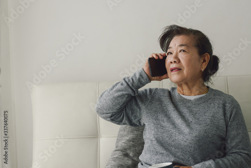 Happy Asian senior woman talking a phone and holding drink cup, stay home stay safe concept.