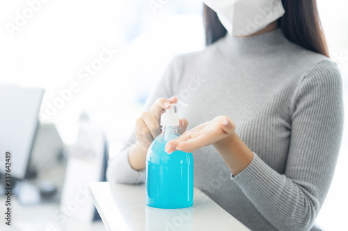 Woman wearing face mask protective for spreading of disease virus SARS-CoV-2 and hand wash cleaning by alcohol gel in office working for protection bacteria and virus, Covid-19 Coronavirus concept © sattahipbeach