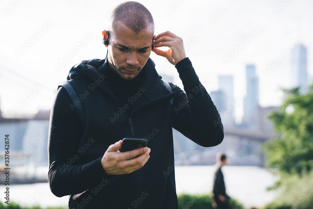 © BullRun - Pensive sportsman walking in park choosing music on phone for training