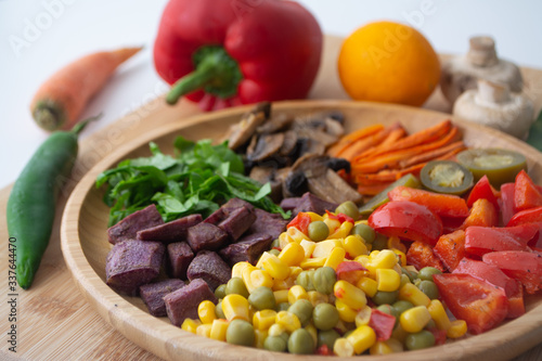 Nutritious and healthy buddha fajita bowl with sweet corn, green peas, red bell pepper, jalapenos, carrots, mushrooms, spinach, beetroot and sweet potatoes surrounded by ingredients and lemon
