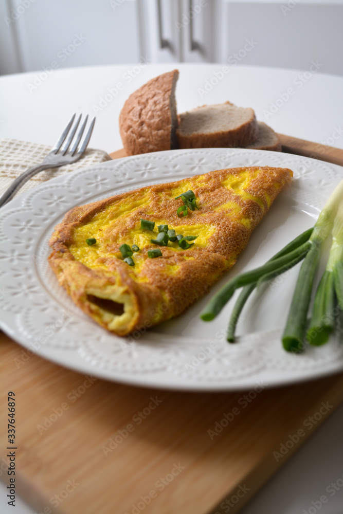 Fluffy breakfast omelette with green spring onions and fresh toast bread on a wooden surface with a napkin and metal fork Fluffy breakfast omelette with green spring onions and fresh toast bread on a wooden surface with a napkin and metal fork