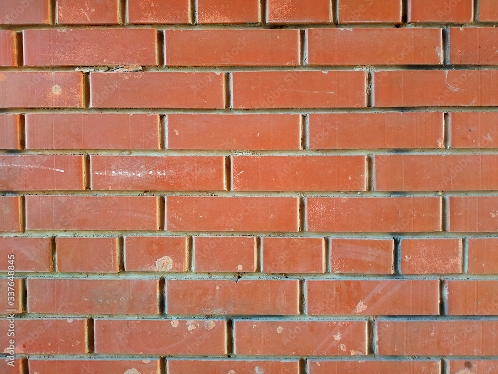 Obraz premium Red brick neutral wall. Smooth laying of brick without retouching. Background for design, construction of houses, fences, obstruction.The concept of reliability and durability.Mortgage and Real Estate