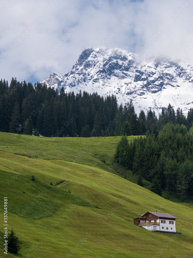 Fresh snow on the summit of Karhorn, green alpine pastures and an isolated house in Lech, Vorarlberg, Austria