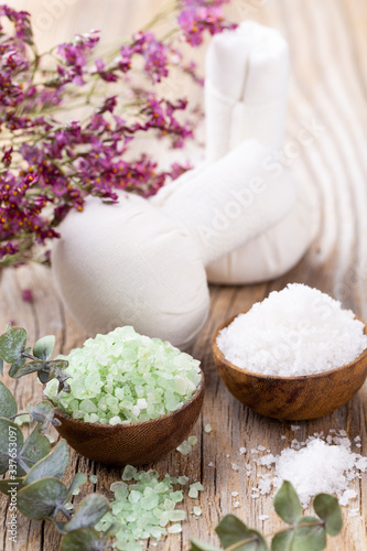 Sea salt in bowl  aroma oil in bottles  Wellness and flowers on grey textured background and flowers on vintage wooden background. Selective focus.