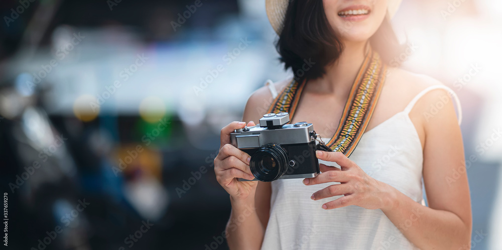 Young woman with retro camera standing outdoors with sunlight.