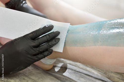 The process of female waxing. Beautician removes wax with hair from female legs.