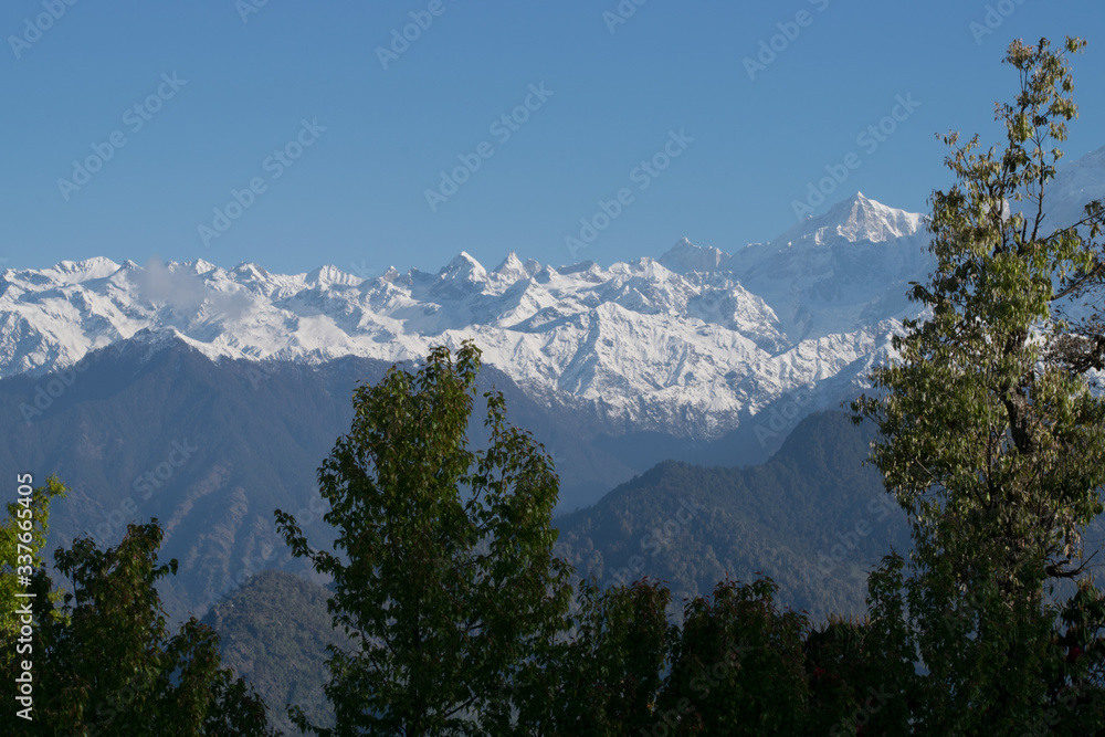 Spectacular view of snow clad mountains surrounded by forest and dramatic clouds in the sky. Amazing landscape during spring trek to Deoria lake in Uttarakhand (India).
