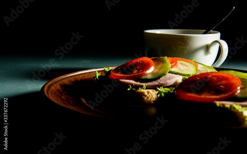 delicious sandwiches with ham, lettuce, cucumber, tomato and a Cup of coffee on a dark background.