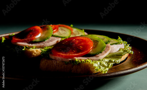 delicious sandwiches with ham, tomato, cucumber and lettuce on a green background