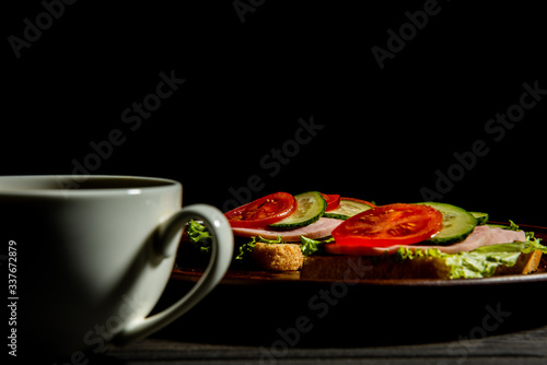 delicious sandwiches with ham, lettuce, cucumber, tomato and a Cup of coffee on a dark background.