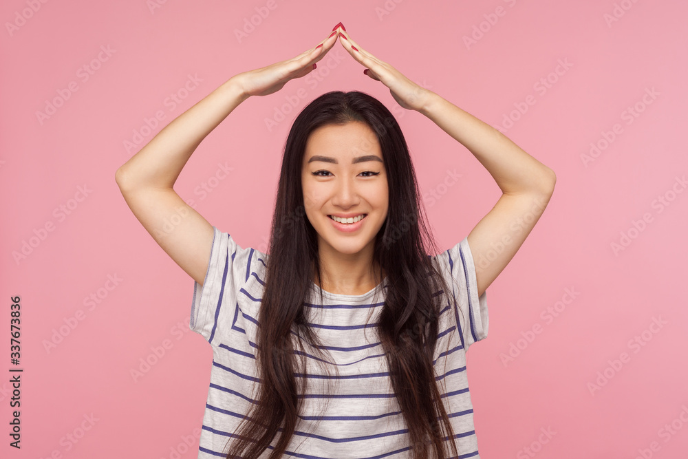 Protected life, insurance. Portrait of happy girl with brunette hair in striped t-shirt feeling safe under house roof gesture and smiling at camera. indoor studio shot isolated on pink background Protected life, insurance. Portrait of happy girl with brunette hair in striped t-shirt feeling safe under house roof gesture and smiling at camera. indoor studio shot isolated on pink background